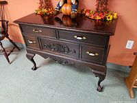 Full view of the dark stained solid wood sideboard chest showing the ornate carvings, brass and ceramic drawer pulls, and claw feet.
