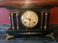 Front view of vintage Waterbury mantle clock showing round numeric dial and decorative columns on black wood case.