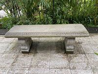 Full view of the cement bench showing rectangular top, decorative edging and two solid carved legs.