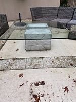 The full glass top resting on the cement base with outdoor wicker chairs in background showing table shape and size.