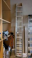 Full view of aluminum extendable ladder leaning against wall in garage with approximate 10 ft short length.