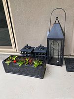 Photo of two cast iron lanterns, tall metal and glass lantern, and rectangular fiberglass planter with plants