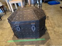 Full view of the metal trunk showing its octagonal shape, domed lid, rivet decoration, and lock closures.