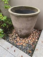 Full side view of large round cement planter placed outdoors on decorative stones.