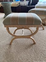 Front view of upholstered stool showing square cushioned seat with green and beige stripes, painted wood frame and curved legs.