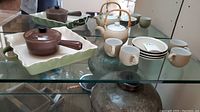 Photo showing full tea set with teapot, 4 cups with saucers, casserole dish and pot on glass shelves