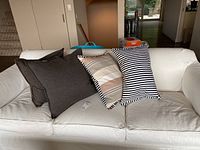 Four throw pillows displayed on a white couch, showing two brown pillows and two striped pillows.