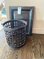 Rectangular metal tray and open grid metal basket with handle placed on wooden floor.