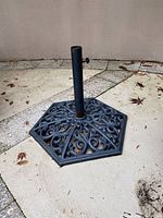 Full view of heavy hexagonal cast iron umbrella stand base showing ornate scroll and floral pattern with central umbrella tube.