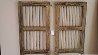 Two vintage shutters made of metal rods framed by distressed wood, hanging on a wall.