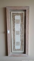 Full view of the shadow box wall art showing fabric panel in center with textured beige and white fabrics within a rustic light wooden frame.