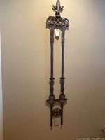 Full view of tall cast iron wall hanging mounted on a wall showing entire length and design.