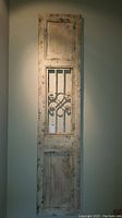 Front view of the tall, narrow wooden wall art panel with distressed paint and central metal grille.