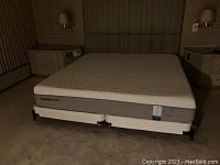 Full bed setup with mattress, box springs, and frame, flanked by two nightstands and wall lamps