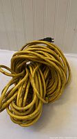 Yellow 100 ft extension cord coiled with visible black plug end against a white background.