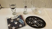 All lot items displayed including flag in bag, 2 pilsner glasses, glass bowl, and cast iron trivet.