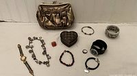 Full lot overview showing the Anne Klein watch, assorted bracelets, ring, heart-shaped trinket box, and metallic evening bag.