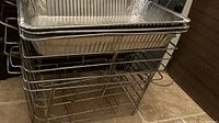 Stack of metal wire chafing racks with rectangular aluminum pans inside, showing structure and handles