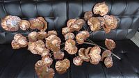 Full view of copper metalwork wall hanging showing many curled and textured copper leaves arranged on thin stems over a black leather background.