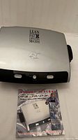 Top view of the George Foreman grill with the recipe manual beside it showing the grill's logo and signature on the lid.