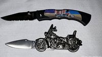 Photo showing the folding knife with black handle decorated with an American flag and motorcycle graphic, blade partially open.