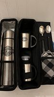 Full view of open coffee kit case showing thermos, two mugs, two spoons, napkins, and mesh pockets