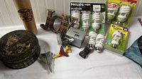 Photo of various items including multiple spiral CFL and incandescent bulbs in packages, a wooden baseball bat pencil holder with 'Dad' etched, a metal 'Joy' sign, and several small models of planes and cars.