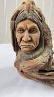Front close-up of the Native American male face with painted markings and eagle feather headdress in the sculpture.