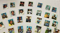 Overview photo showing 26 assorted baseball cards laid out on a flat surface, featuring a mix of individual player portraits and action shots.
