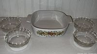 Lot showing one CorningWare square casserole dish La Marjolaine pattern and four clear Pyrex round bowls.