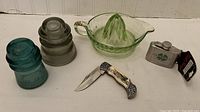 Full view of all items: utility insulators, green glass juicer, folding knife, and Irish flask.
