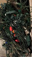 Photo showing multiple tangled vintage Christmas light strands with green wiring, different bulb colors including red, orange, and clear, and diverse socket styles.