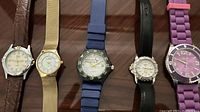 Photo showing five women's watches arranged side by side on a table with clear view of bands and dials
