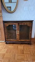 Front view of wooden side cabinet with two glass front doors, brass handles, and decorative base.