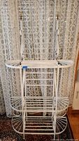 Front view of white metal bakers rack showing three tiers and decorative scrollwork