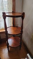 Photo of the three-tiered round wood stand showing the full height and the turned wooden legs supporting the round shelves.