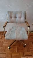 Front view of fabric upholstered retro rolling chair with button tufted backrest and wooden armrests.
