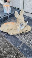 Deer statuette lying down with a bird perched on its neck, placed on textured ground.