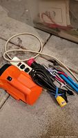 Orange electric device, flashlight, multiple hand tools with blue and red handles on concrete floor near white power strip