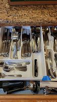 Drawer with flatware forks, knives, and spoons with matching decorative handles along with extra utensils below.