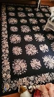 Full view of large woven floral area rug showing black background with repeating pink floral bouquet pattern and border detail.