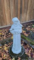 Full view of the garden religious statue standing on octagonal base among fallen leaves and mossy stone.