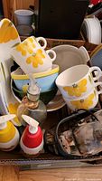 Mixed kitchen and serving bowls with floral designs stacked in a box along with condiment dispensers and glass bottles.