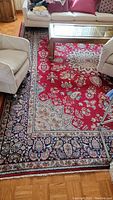 Overall view of rug under living room furniture showing red field, central medallion, and border.