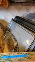 Stack of various rectangular cookie sheets and baking trays with a metal wire cooling rack on top.