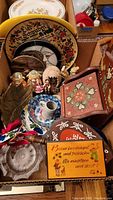 Image showing wooden tole painted box, several hand painted plates with German text, crystal dishes, figurines of children, and a blue floral cat bowl.