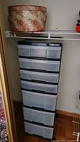 Photo showing the tall plastic drawer organizer on wheels with six transparent drawers and black handles, placed on floor.
