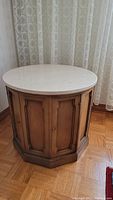 Side view of the round wooden side cabinet with stone top, showing octagonal base and door detailing