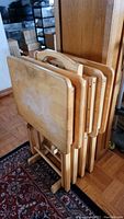 Set of four light wood TV trays with holder, positioned upright on a floor rug. Visible surface wear and staining on trays.