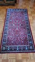Full view of a red area rug with floral motifs and navy patterned border on hardwood floor.